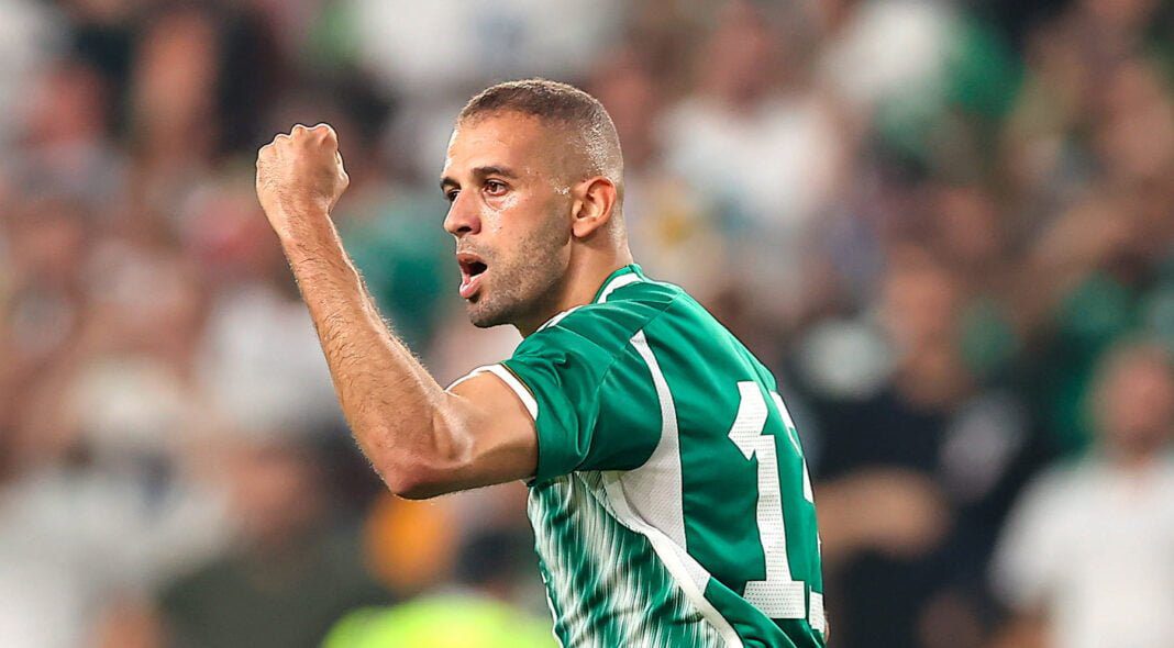 Islam Slimani en action, portant un maillot vert et blanc lors d'une compétition de football.