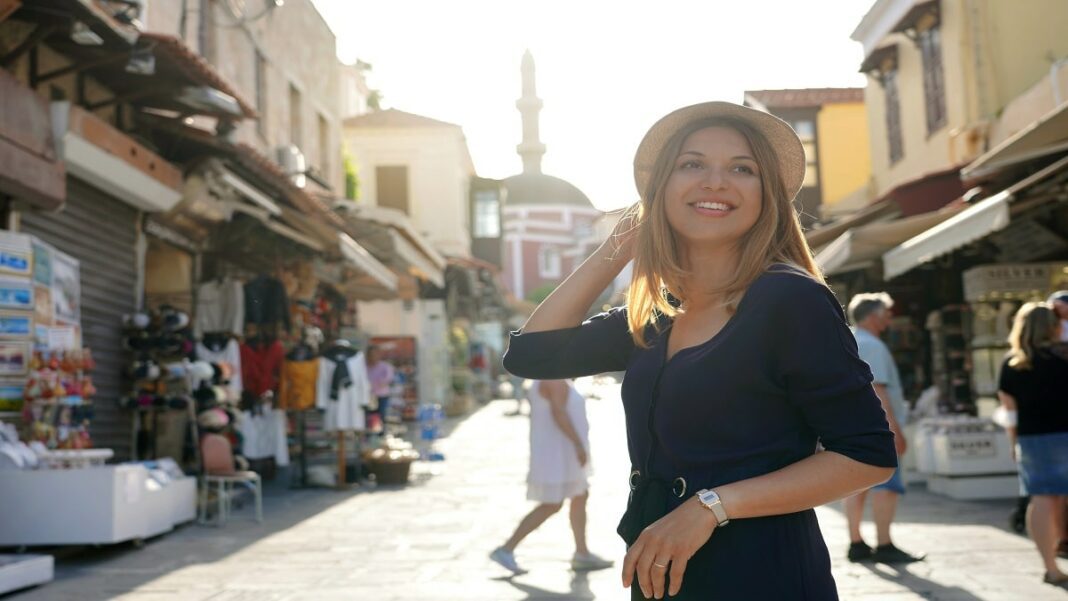 Algérie : Fit Claire témoigne de l’ultra-protection des touristes lors de son périple à Oran Femme souriante à Oran, marché animé avec boutiques colorées.