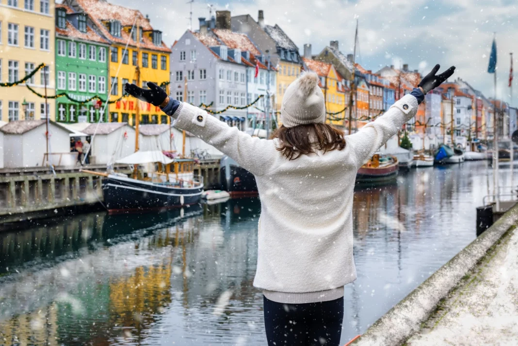 Voyage en Europe : Découvrez les 4 destinations les moins chères en hiver Femme admirant les maisons colorées de Copenhague sous la neige.