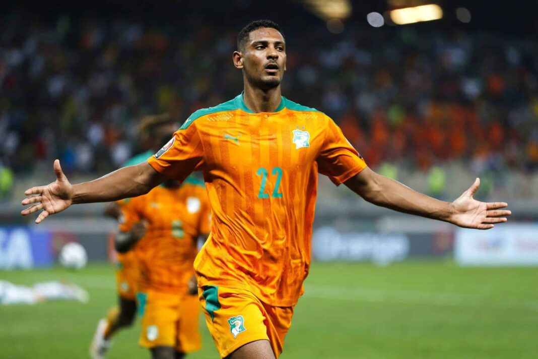 Footballeur ivoirien en maillot orange avec bras ouverts sur le terrain.