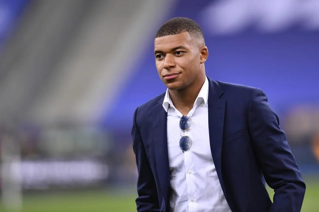 25 ans d’existence célébrés ce 20 décembre, le salaire de Mbappé dévoilé Kylian Mbappé portant un costume lors d'un événement sportif.