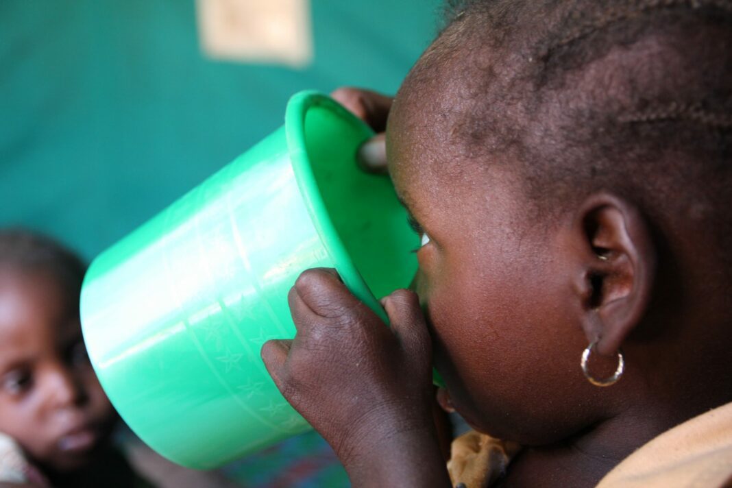 Enfants migrants refoulés d’Algérie vers le Niger : Un périple difficile vers Agadez Jeune enfant buvant dans un gobelet vert, contexte d'enfants migrants.