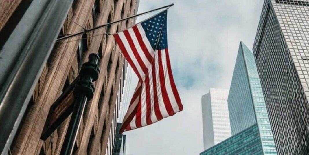 Programme SLP 2024 : Opportunité exceptionnelle pour les étudiants Algériens aux USA Drapeau américain flottant devant des gratte-ciel modernes.