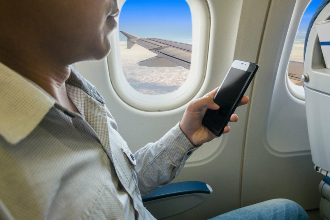 Utilisation du smartphone en avion Homme utilisant un smartphone en vol, vue de l'intérieur de l'avion.