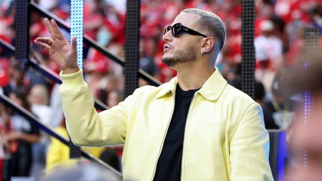 DJ Snake lors d'un concert au Stade de France, portant des lunettes de soleil et un manteau jaune.