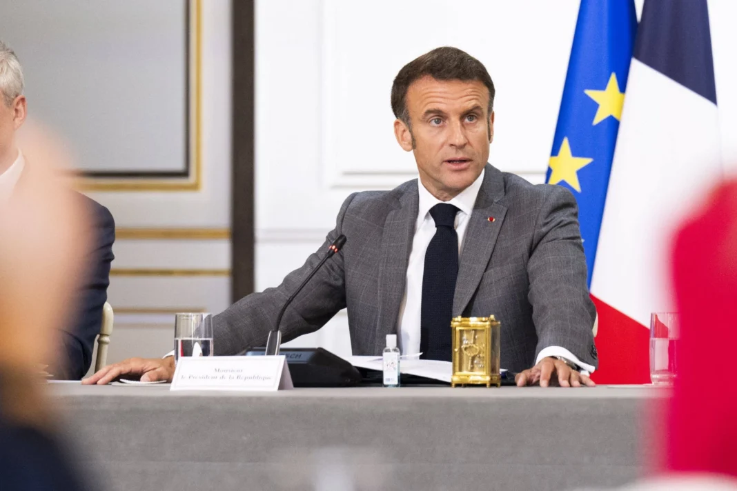 Loi d’immigration en France : Emmanuel Macron mène une démarche de sage Emmanuel Macron à une réunion officielle avec drapeaux français et européens en arrière-plan.