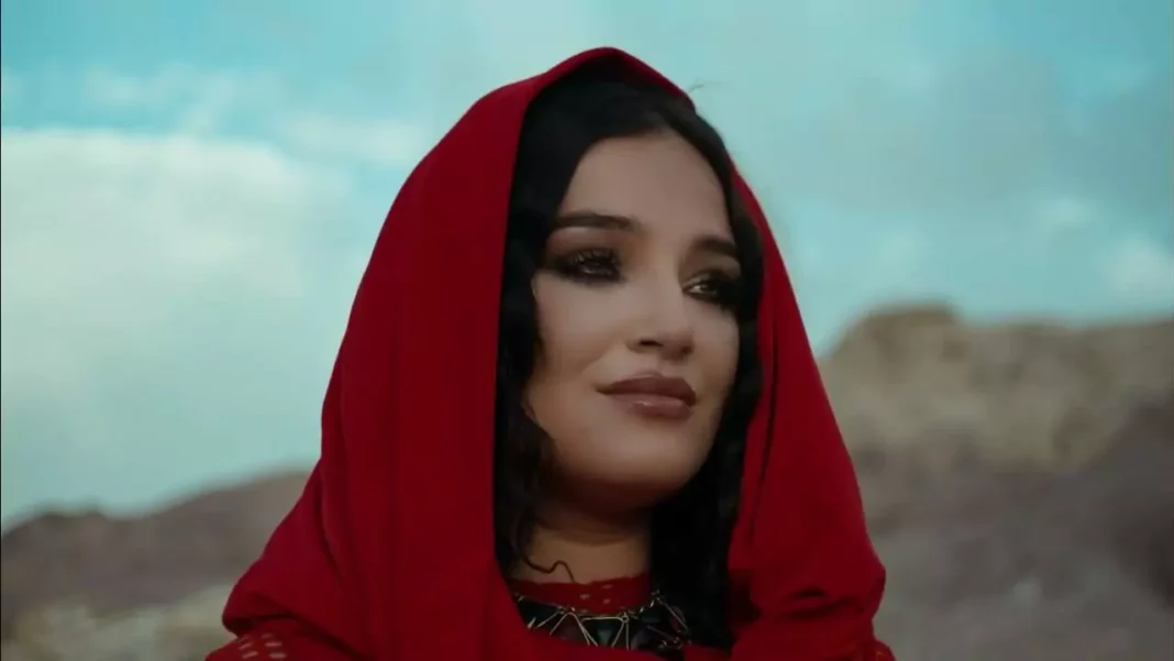 Enfin! Numidia Lezoul touche le faîte, grâce à ceci… Numidia Lezoul avec un voile rouge dans un décor désertique.