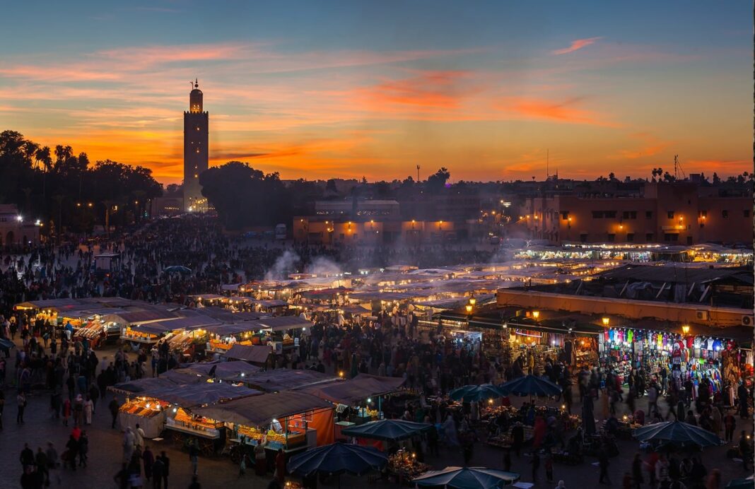 Marché animé au coucher du soleil à Marrakech avec foule et stands colorés.