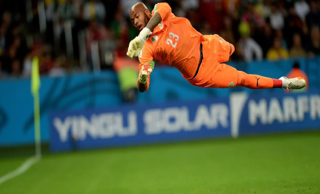Rais Mbolhi exclu de la liste élargie de Djamel Belmadi ? Rais Mbolhi plonge pour arrêter un tir lors d'une rencontre de football.
