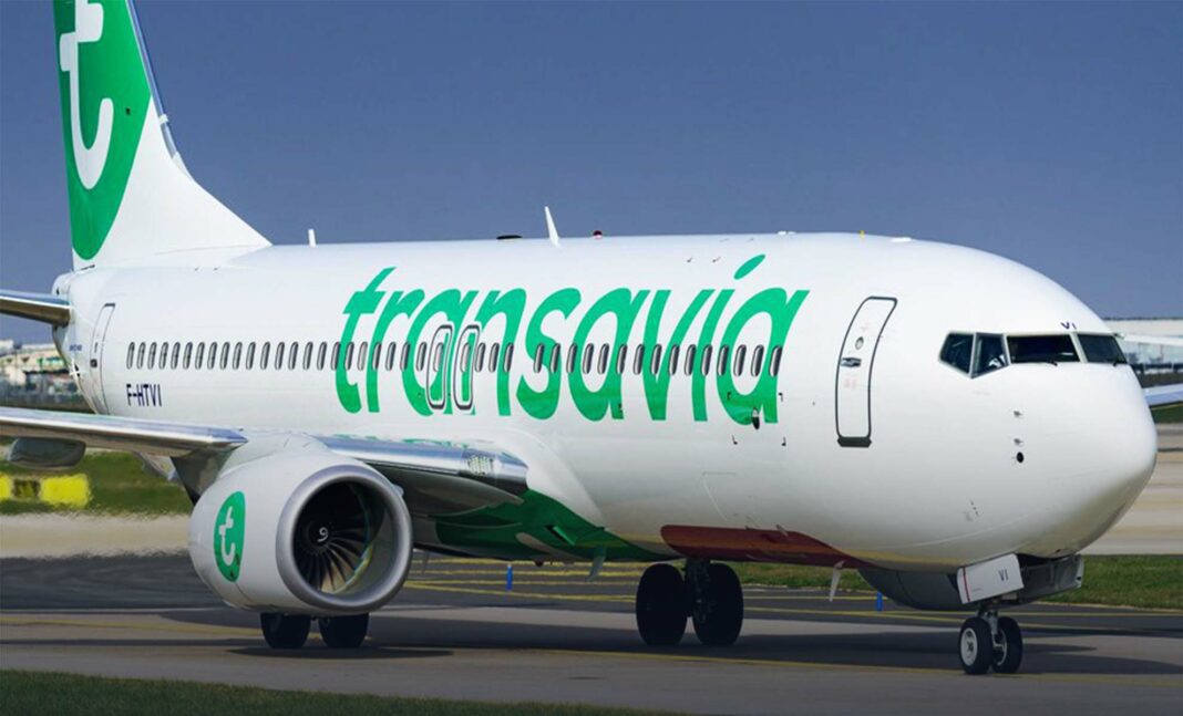 Avion Transavia blanc avec logo vert en atterrissage sur piste.