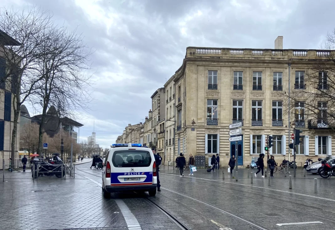 Violences conjugales à Bordeaux : Un Algérien sous OQTF en fuite après avoir agressé sa femme à coups de couteau Vue de la rue à Bordeaux avec un véhicule de police et des passants.