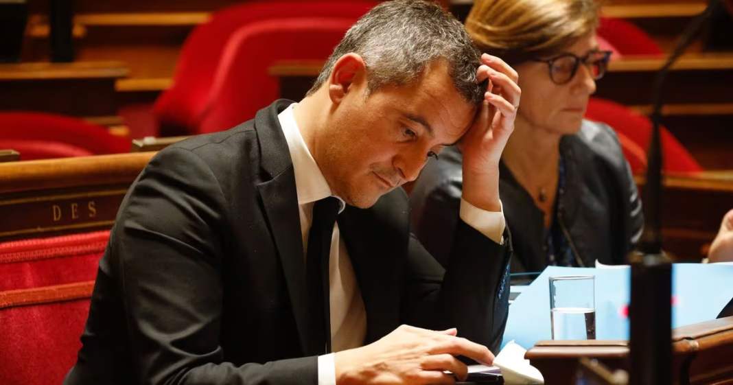 La France durcit sa politique d’immigration : Expulsions accélérées et conditions restrictives Homme en costume noir, assis, semble stressé ou concentré en séance parlementaire.