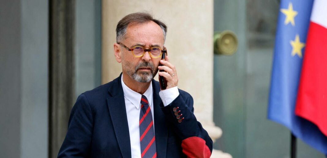 OQTF – Robert Ménard et l’Opposition à un Mariage : Entre Soupçons de Mariage Blanc et Contestation Juridique Homme en costume parlant au téléphone devant drapeaux français et européen.