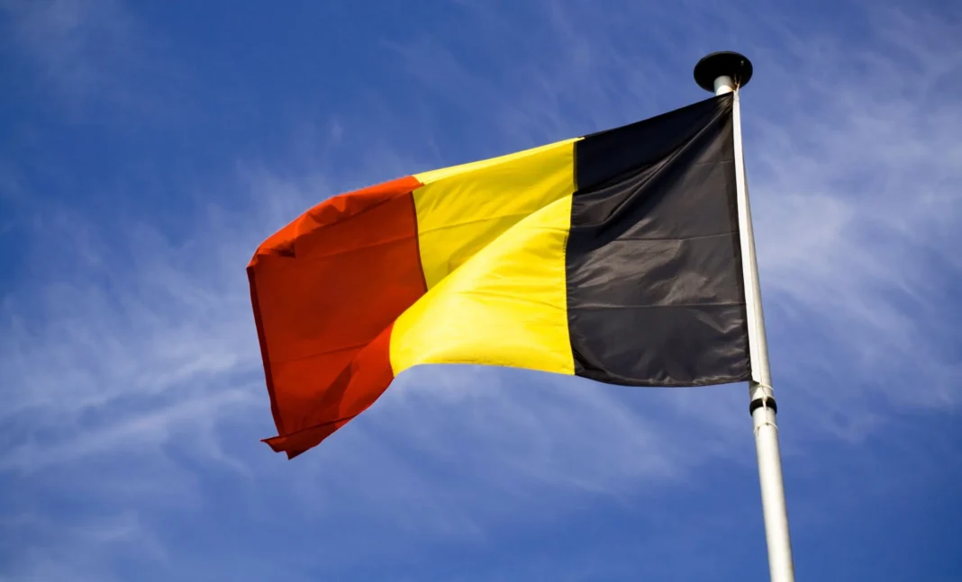Drapeau belge vibrant dans le ciel bleu avec nuages blancs.