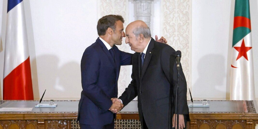 Rencontre diplomatique Algérie-France Deux hommes en costume se serrent la main lors d'une rencontre officielle.