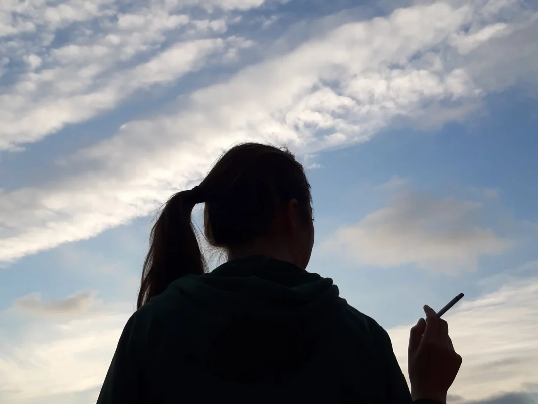 Consommation du Tabac par les femmes : une journée du 8 mars propice à une sensibilisation de la gent féminine Femme de dos utilisant un smartphone au coucher du soleil.