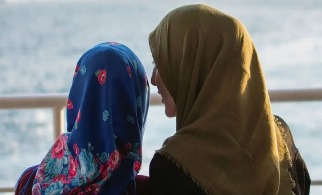 France : elle refuse de retirer son voile et agresse son enseignante Deux femmes avec hijabs regardant l'eau, conversation sérieuse.