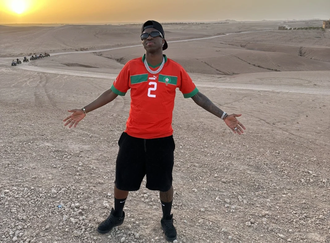 Racisme au Maroc : Vinicius Junior, de nouveau face à ses démons de l’occident Jeune homme portant un maillot de football dans un désert au coucher du soleil.