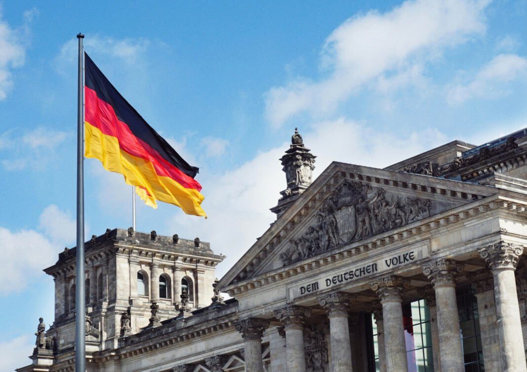 L’Allemagne Ouvre ses Portes aux Travailleurs Qualifiés : Ce que Vous Devez Savoir Drapeau allemand flottant devant un bâtiment historique en Allemagne.