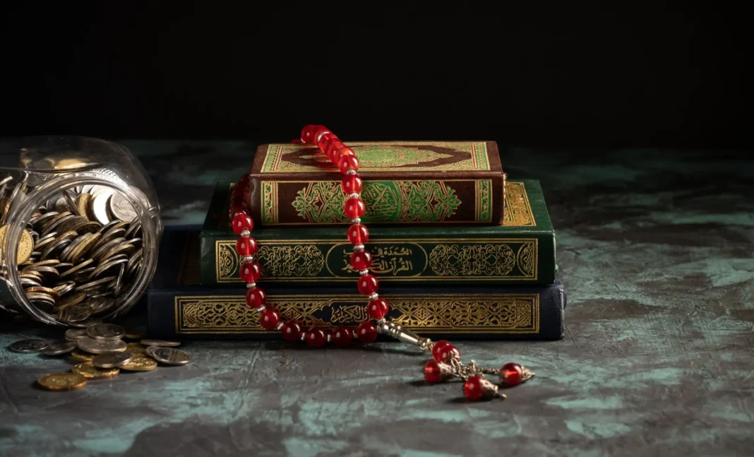 Ramadan en France : Montants de la Zakat el-Fitr et de la Fidyah dévoilés par la Grande mosquée de Paris Coran avec perles de prière rouges et pièces de monnaie sur une surface sombre.