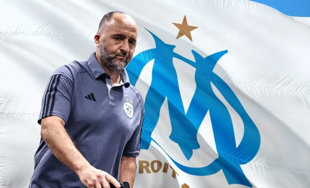 Djamel Belmadi devant le logo de l'OM lors d'une conférence de presse.