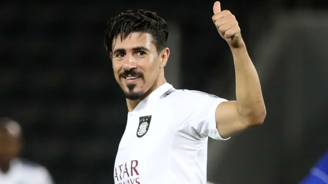 Incroyable! Il met Baghdad Bounedjah au dessus de Messi et Ronaldo : la toile s’enflamme! Footballer Baghdad Bounedjah en tenue blanche, saluant la foule.