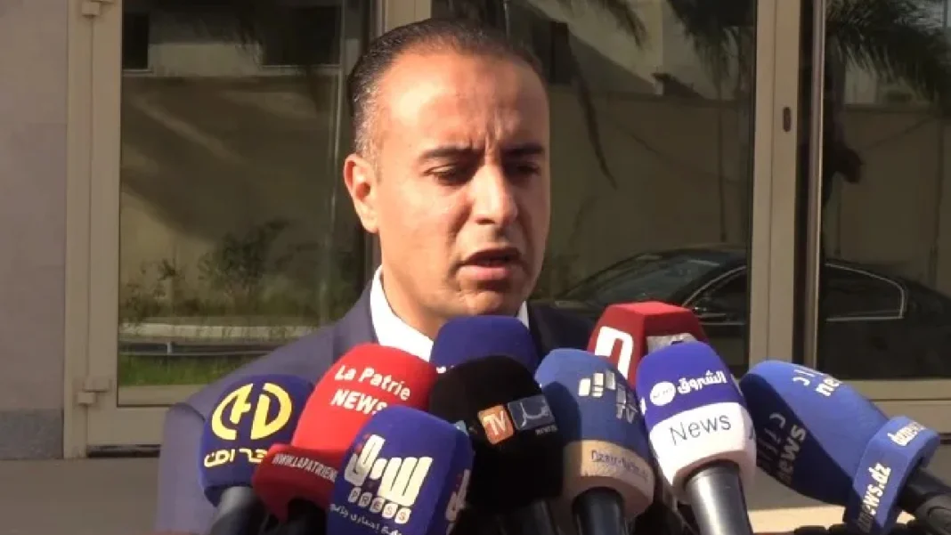 Invité spécial pour Walid Sadi : le foot algérien s’apprête à vivre un ère historique Walid Sadi parlant à la presse avec plusieurs microphones.