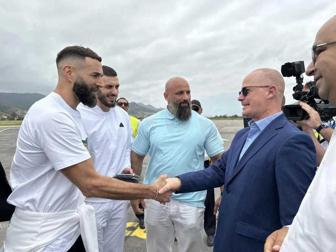 Karim Benzema serre la main d'un homme en costume lors d'une visite en Algérie.