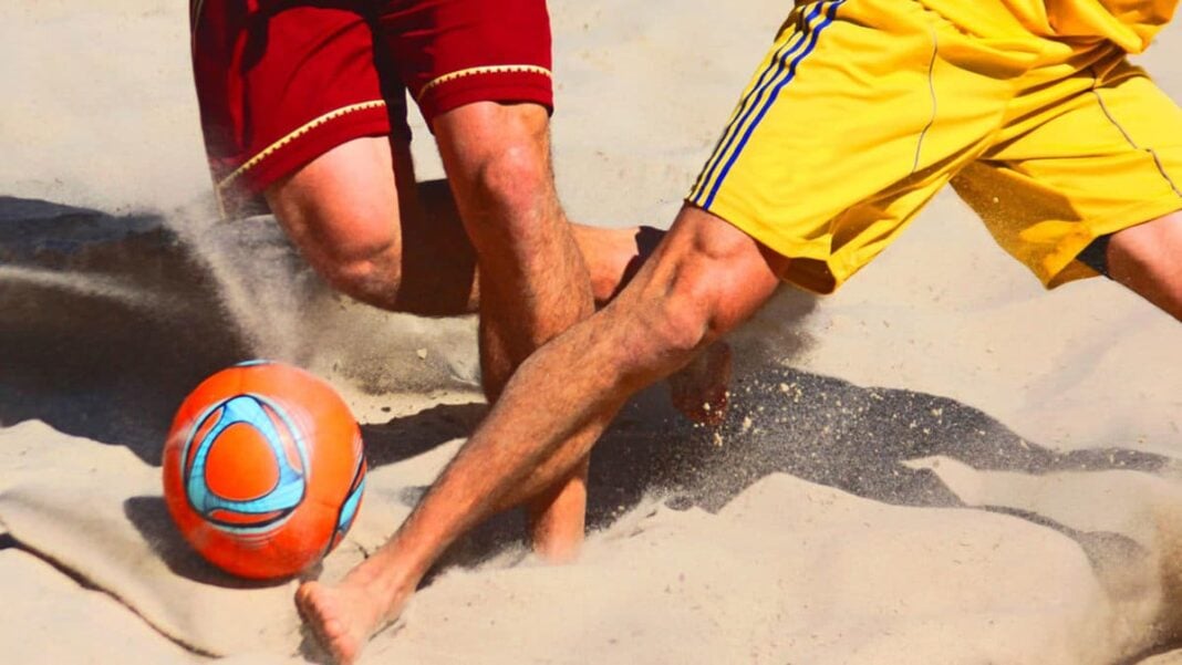 Beach Soccer : Absentéisme à la CAN 2024, la FAF organise un tournoi national Joueurs de beach soccer en action sur la plage avec un ballon orange.
