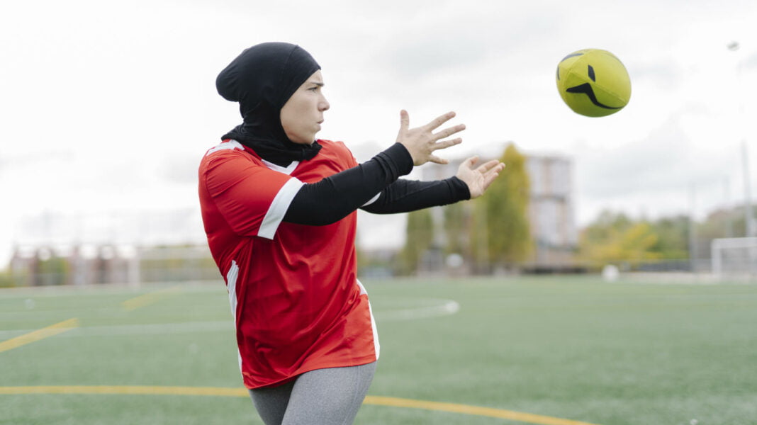 Femme musulmane en hijab jouant au football sur un terrain.