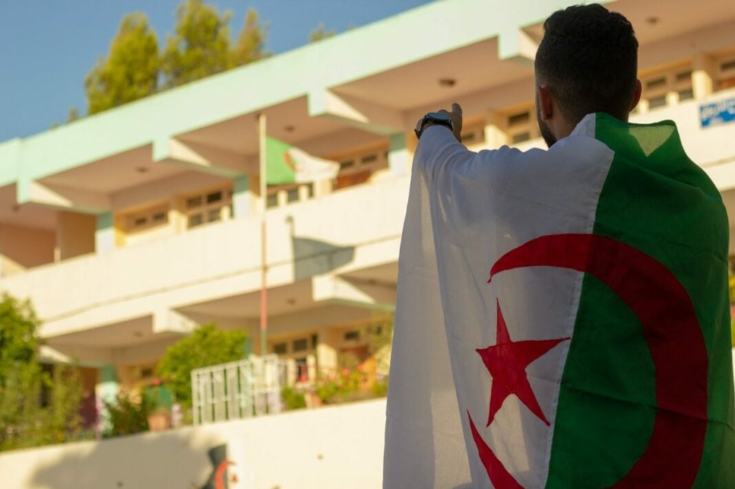 Acquittement historique en Algérie : victoire pour la communauté chrétienne persécutée Homme tenant un drapeau algérien devant un bâtiment moderne.