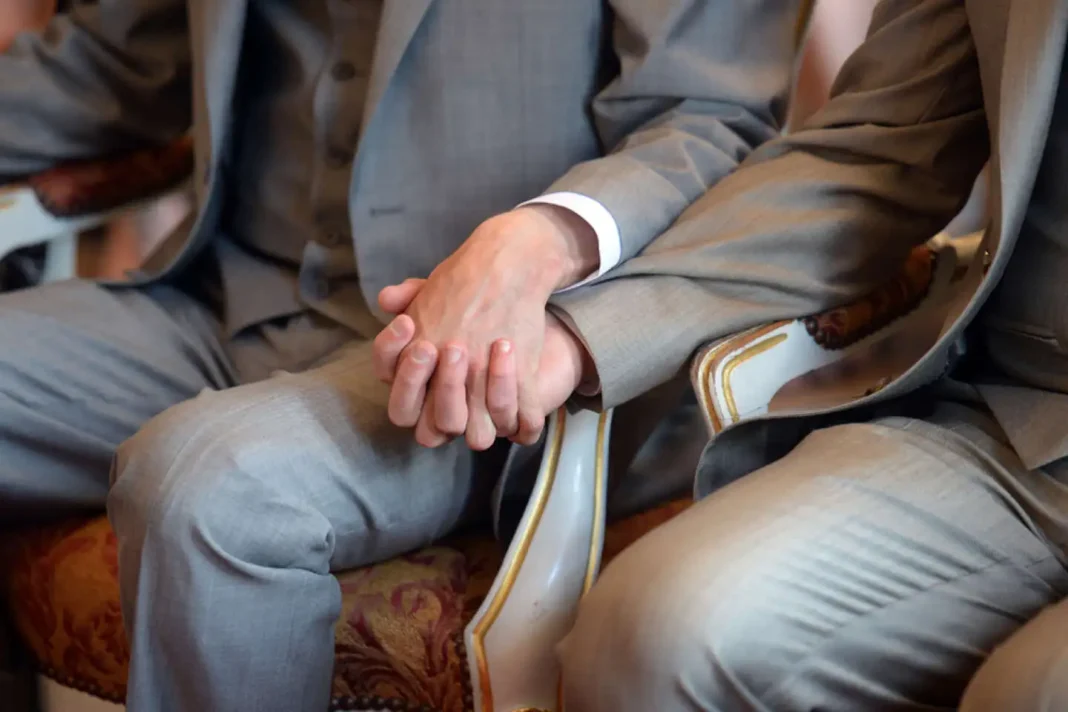 Mariage homosexuel : le Maroc oppose un « NON » mordicus Deux hommes en costume se tenant la main lors d'une cérémonie.