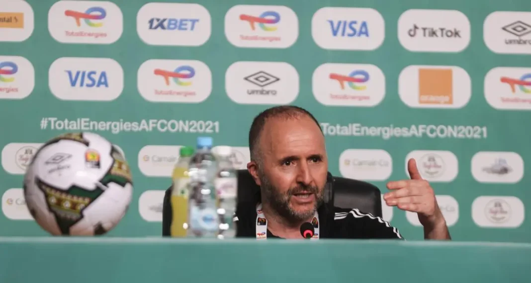 Djamel Belmadi en conférence de presse Djamel Belmadi lors d'une conférence de presse avec le logo de la CAN 2021 en arrière-plan.