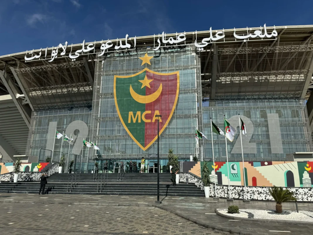 Le stade Ali La Pointe de Douera sur une pente ascendante! Un passé déshonorant désormais rangé aux oubliettes Stade Ali La Pointe à Douera avec drapeaux et logo MCA.