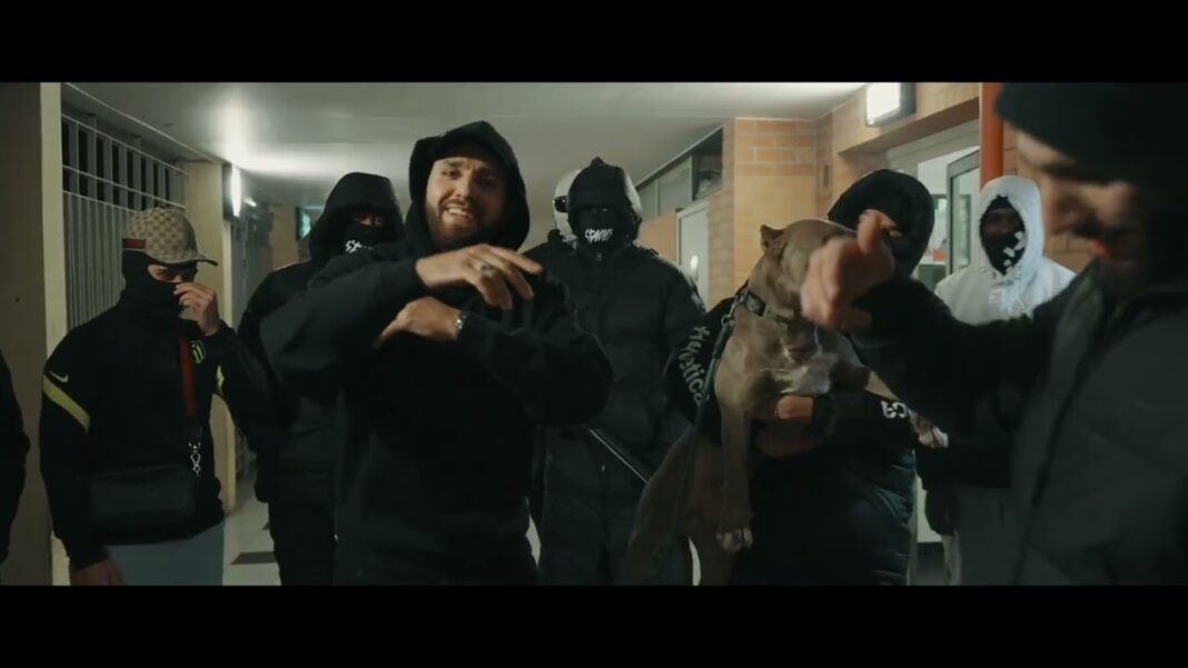 S’TANO : Un artiste algérien au style unique, entre exil et succès musical Groupe de jeunes hommes en tenue sombre, certains masqués, dans un couloir urbain.