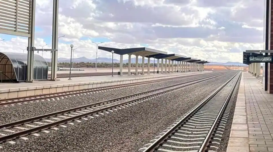 Gare en construction avec voies ferrées et plateforme d'attente.