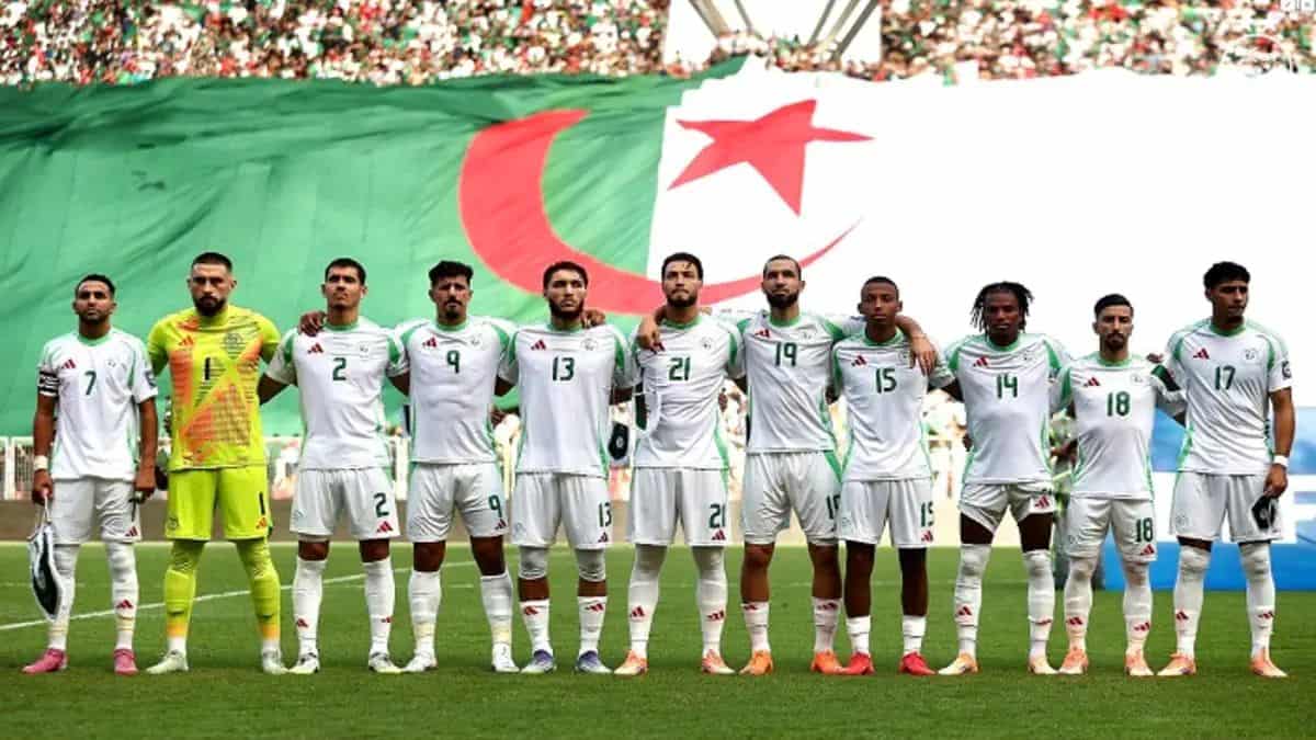 Équipe d'Algérie de football en action Les joueurs algériens alignés devant un drapeau national lors d'un match.