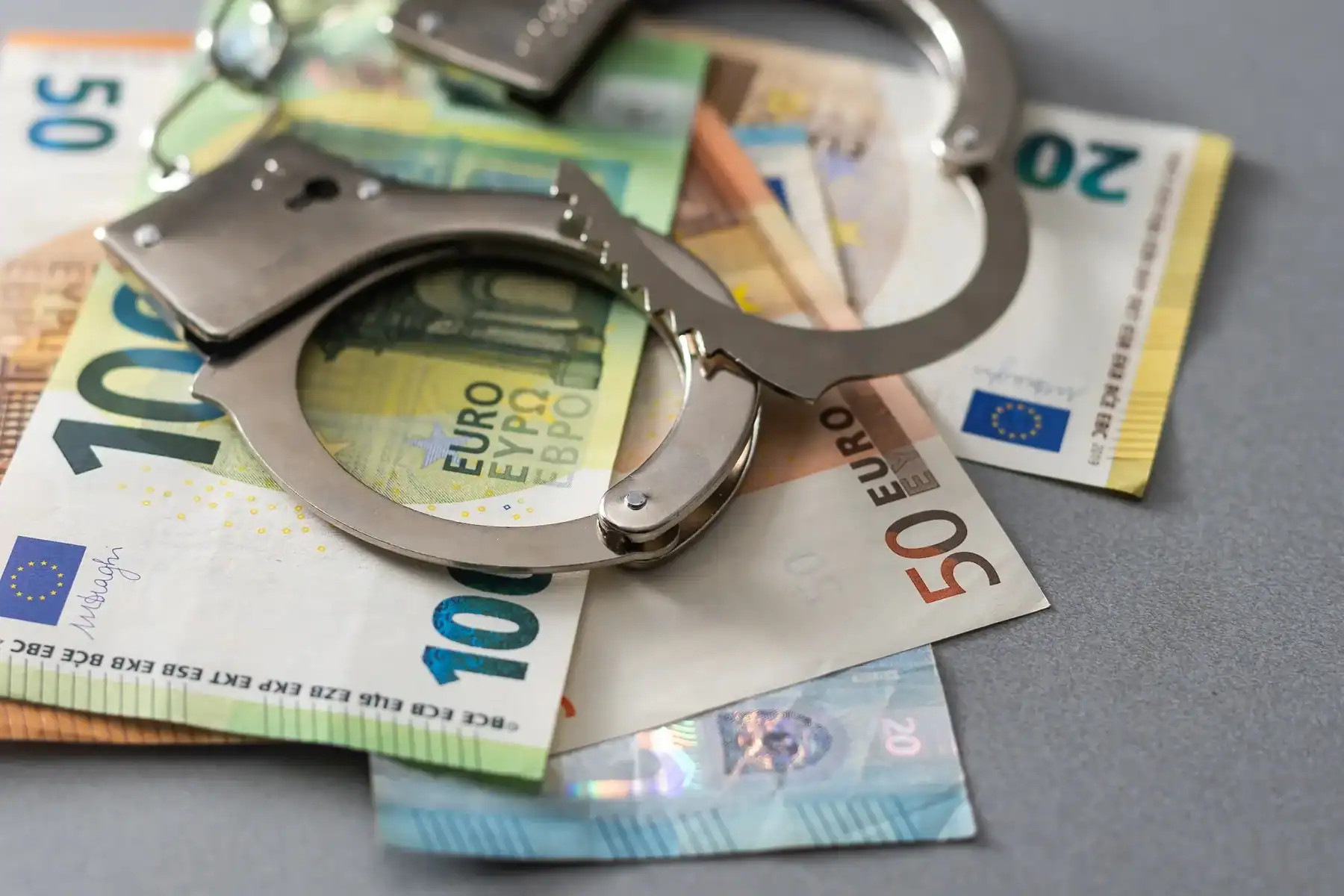 Réseau de fraude aux aides touristiques démantelé Menottes sur des billets de banque euro, illustrant la fraude financière.