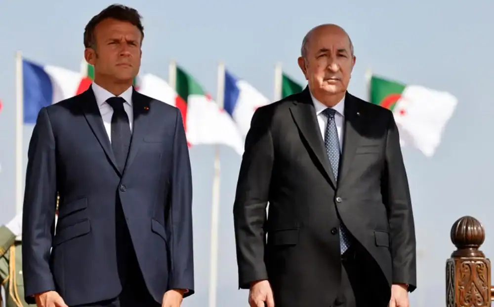 Deux dirigeants en costume lors d'une cérémonie officielle avec drapeaux en arrière-plan.