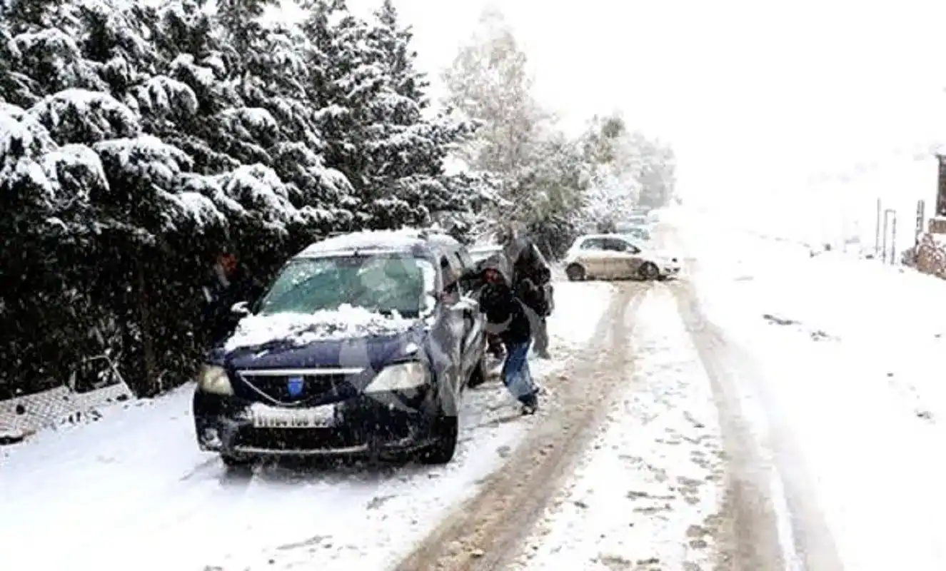 Voiture accidentée sous la neige avec personnes à côté en Algérie.