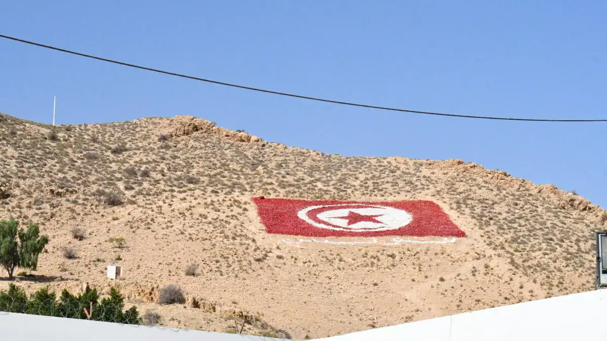 Drapeau tunisien peint sur une colline dans un paysage désertique.