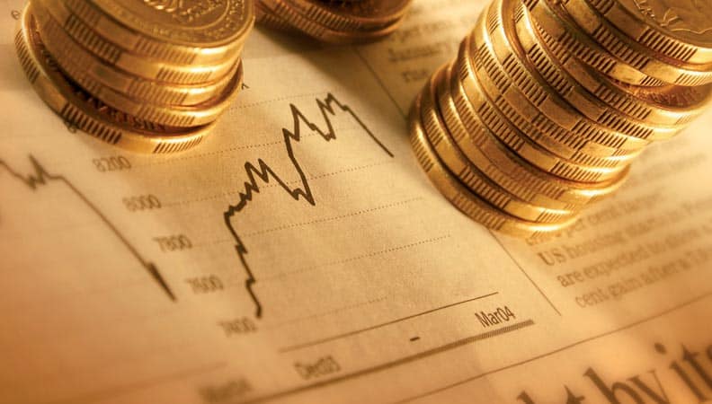Algérie : premiers sukuk souverains pour 2,3 Mds $ émis Stacks de pièces d'or sur graphique financier en arrière-plan.