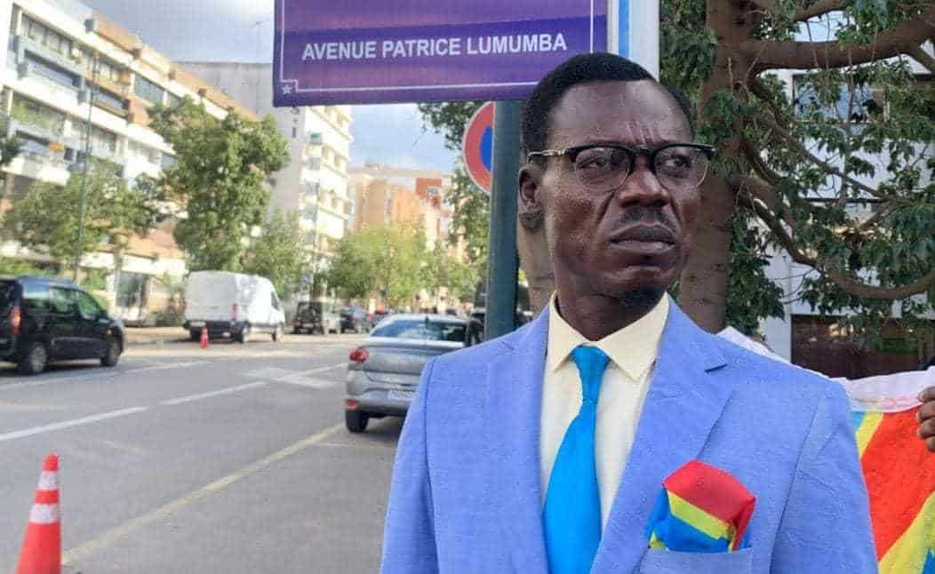 Un invité surprise crée l’événement à l’hôtel des Fennecs Homme en costume bleu avec lunettes devant une rue animée.