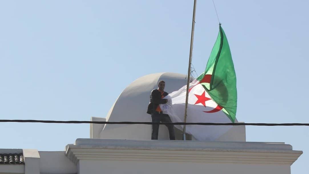 Scandale à Casablanca : le drapeau algérien arraché Homme déployant le drapeau algérien sur un bâtiment à Casablanca.