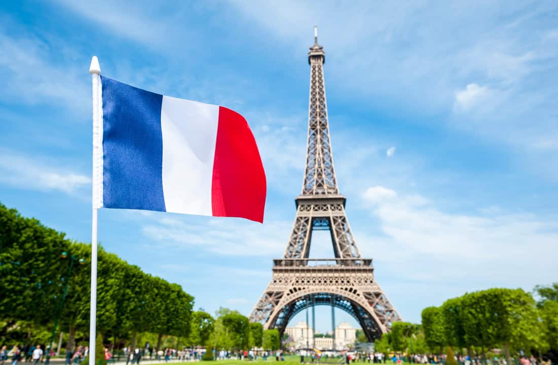 Pourquoi tant d’Algériens choisissent la France aujourd’hui ? Drapeau français flottant avec la Tour Eiffel en arrière-plan.