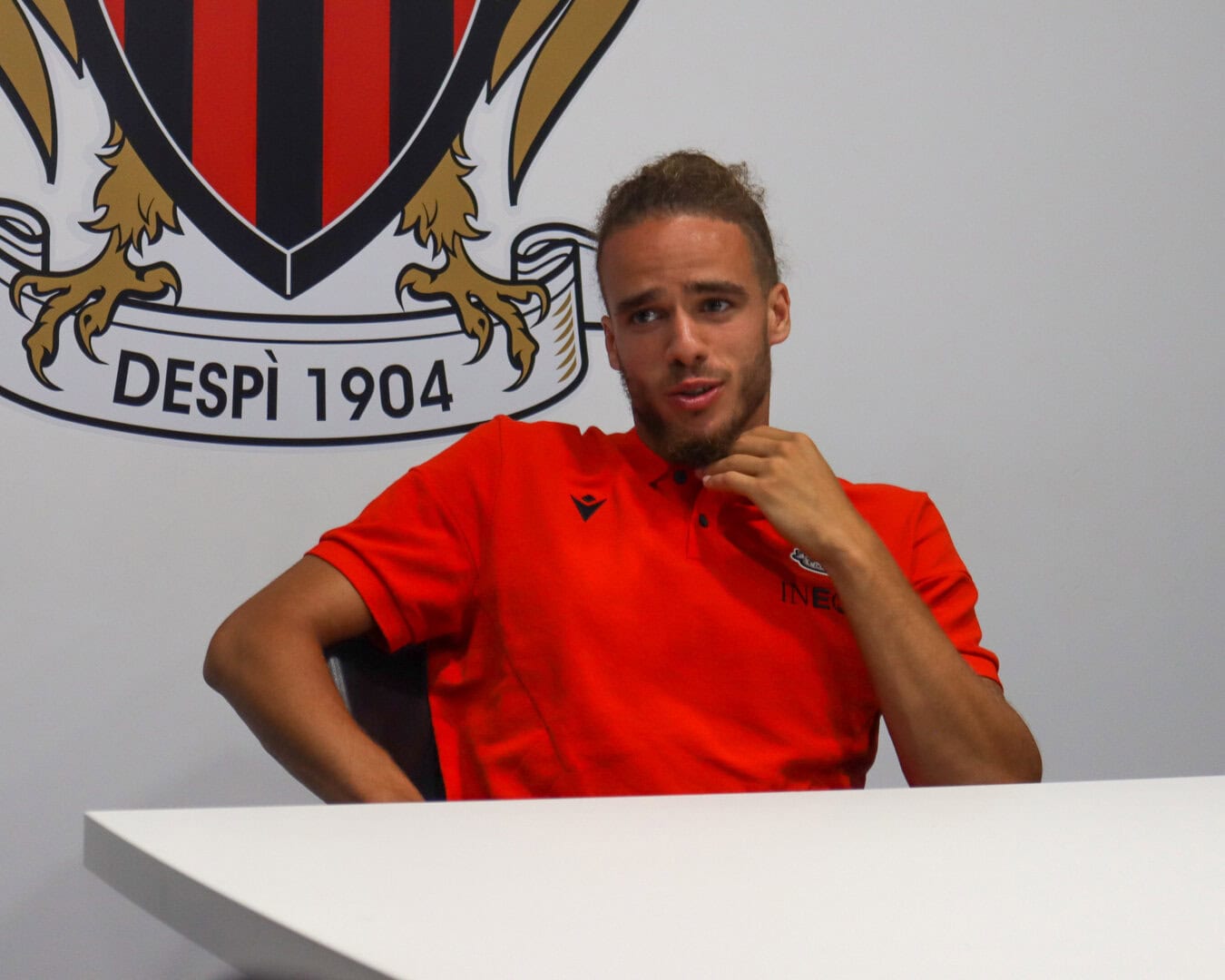 Jeune homme en discussion, portant un maillot rouge, dans un contexte sportif.