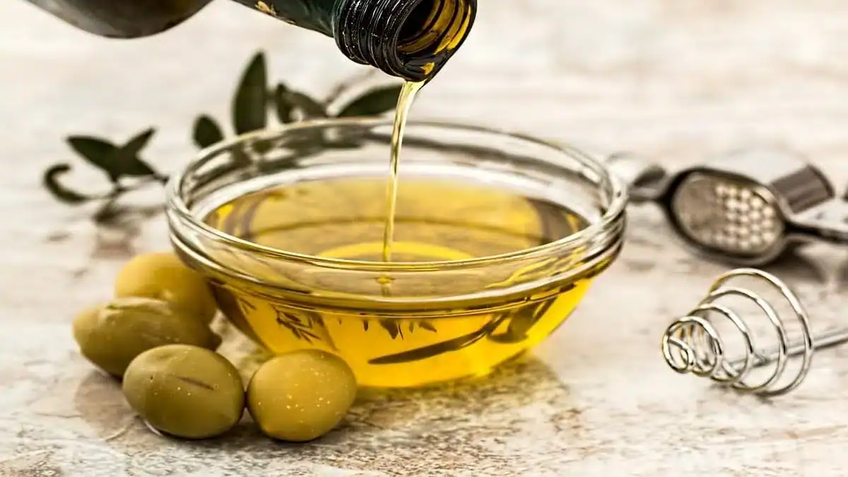 Top 4 des huiles d’olive algériennes plébiscitées en 2024 Huile d'olive versée dans un bol avec olives vertes.