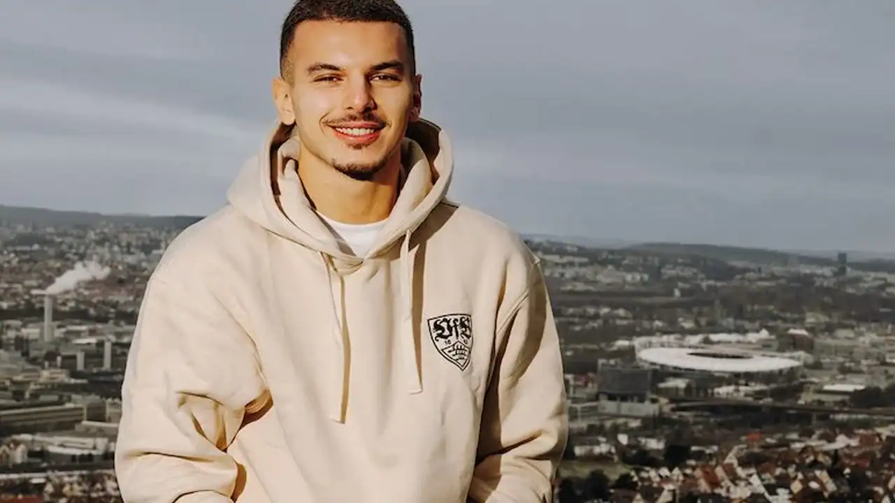 Jeune homme souriant portant un sweat à capuche beige en extérieur.