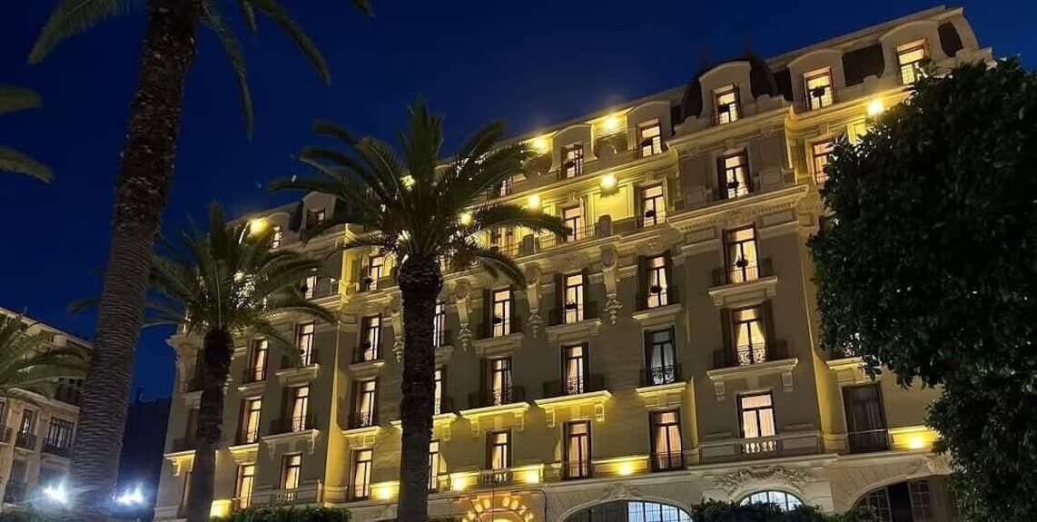 Hôtel élégant avec éclairage nocturne et palmiers en avant-plan.