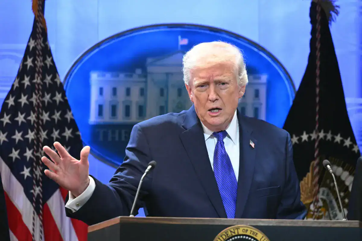Donald Trump parlant à la presse avec drapeaux américains en arrière-plan.